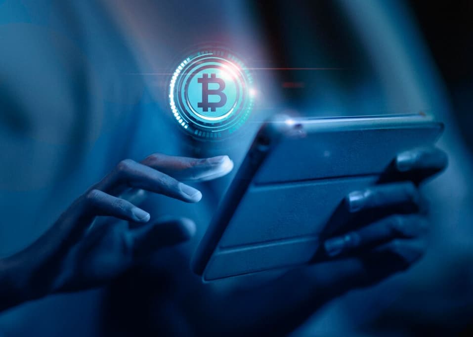 Hands holding a tablet with a floating Bitcoin symbol above it in blue light