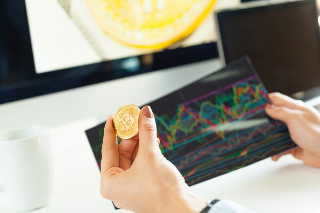Hand holding a bitcoin coin on a background of paper with a graph