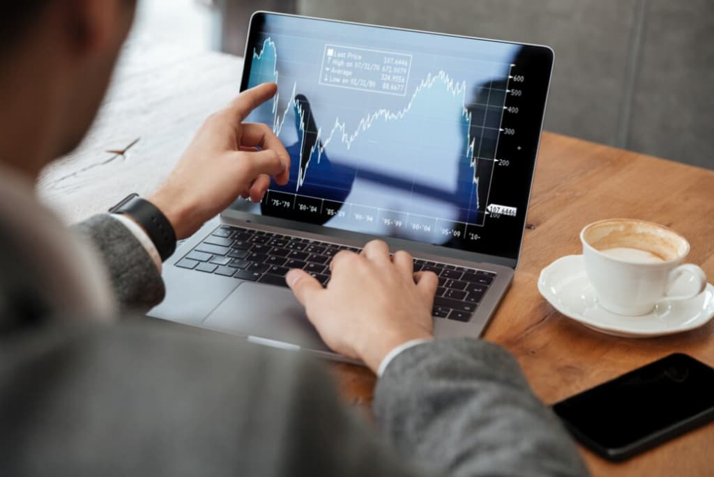 Person analyzing financial graphs on a laptop with a coffee cup